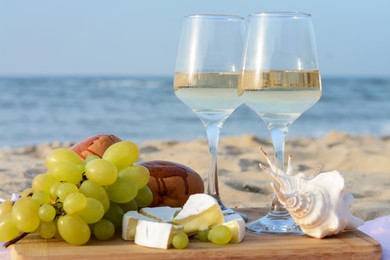 Glasses with white wine and snacks for beach picnic on sandy seashore, closeup
