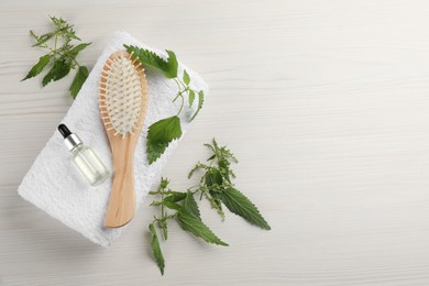 Stinging nettle, extract, towel and brush on white wooden background, flat lay with space for text. Natural hair care