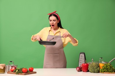 Emotional housewife with vegetables and different utensils on green background