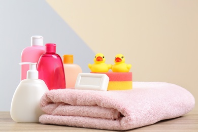 Baby cosmetic products, toys and towel on table against color background