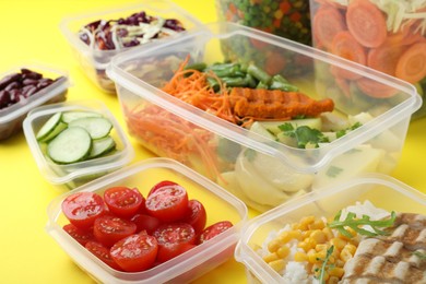 Set of plastic containers with fresh food on yellow background