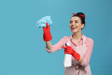 Photo of Young housewife with detergent and rug on light blue background, space for text