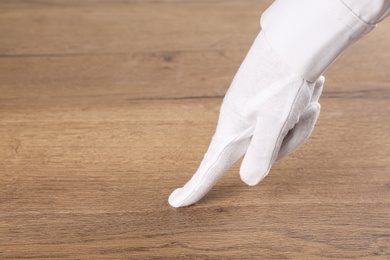Person in white glove checking cleanliness of wooden  table, closeup. Space for text
