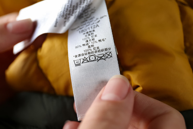 Woman reading clothing label with care symbols and material content on color jacket, closeup