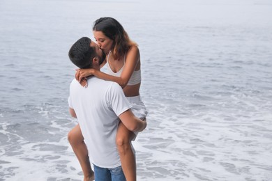 Young couple kissing near sea. Space for text