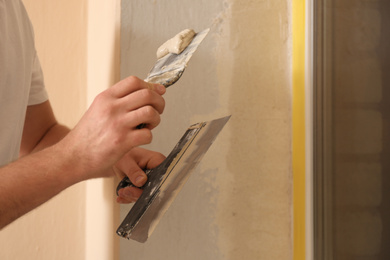 Man plastering window area with putty knife indoors, closeup. Interior repair