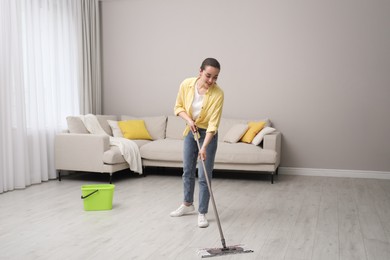 Young woman cleaning floor with mop in living room
