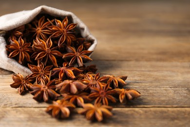Overturned bag with aromatic anise stars on wooden table, closeup. Space for text