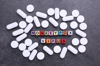 Photo of Words Monkeypox Virus made of cubes and pills on grey table, flat lay