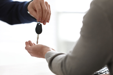 Salesman giving key to customer on light background, closeup. Buying new car