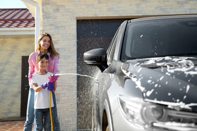 Mother and son washing car at backyard on sunny day
