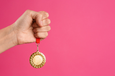 Woman holding golden medal on pink background, closeup. Space for design