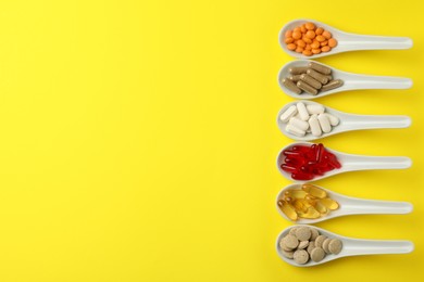 Spoons with different dietary supplements on yellow background, flat lay. Space for text