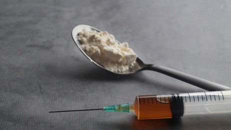 Photo of Spoon with powder and syringe on light grey table, closeup. Hard drugs