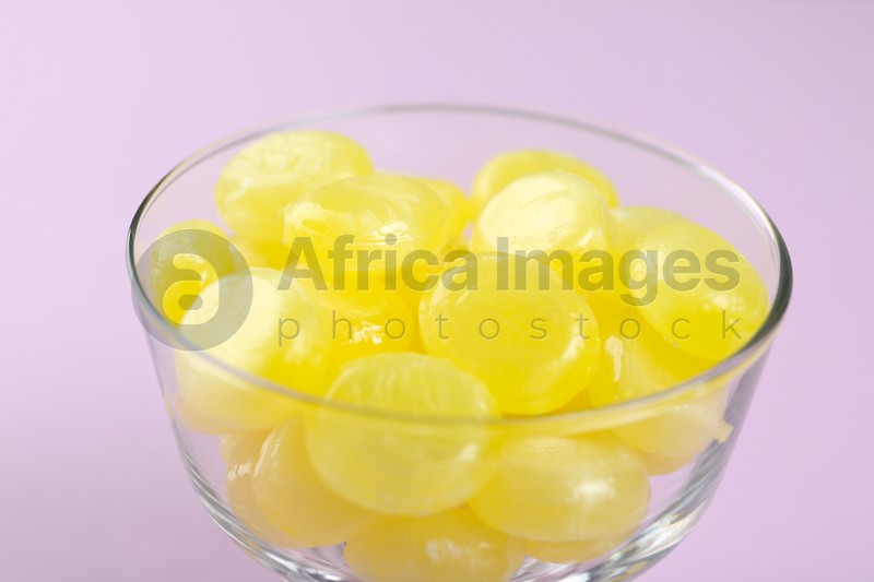 Tasty lemon drops in bowl on violet background, closeup