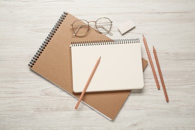 Sketchbooks, pencils, glasses and eraser on white wooden table