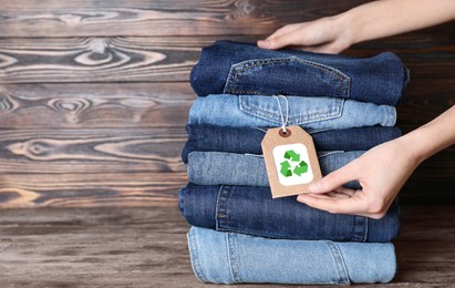Woman and stylish jeans with recycling label on wooden table, closeup. Space for text