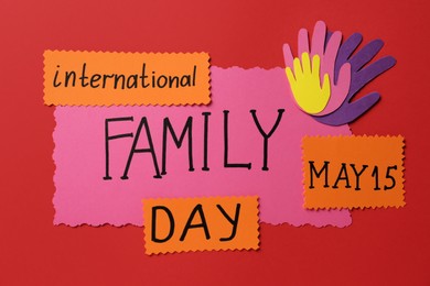Paper palms and cards with text International family day on red background, flat lay
