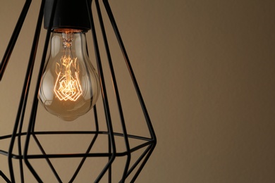 Photo of Hanging lamp bulb in chandelier against brown background, closeup. Space for text