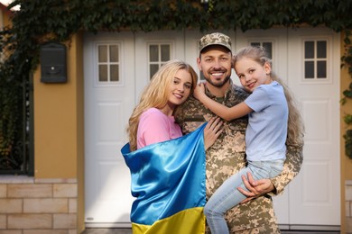 Photo of Soldier in military uniform reunited with his family and Ukrainian flag outdoors, space for text