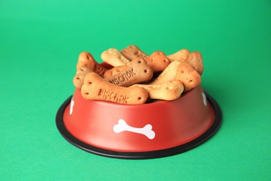 Photo of Bone shaped dog cookies in feeding bowl on green background