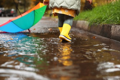 Little girl splashing water with her boots in puddle outdoors, closeup
