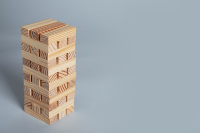Jenga tower made of wooden blocks on grey background, space for text