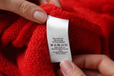 Woman reading clothing label with care symbols and material content on red knitted sweater, closeup