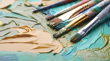 Many brushes on artist's palette with mixed paints, closeup