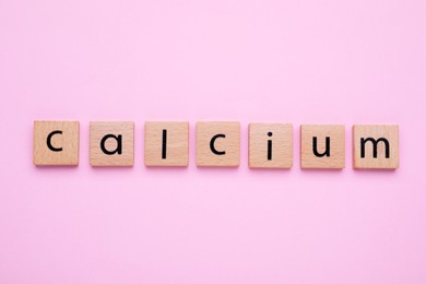 Word Calcium made of wooden cubes with letters on pale pink background, top view