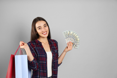Young woman with money and shopping bags on light grey background. Space for text