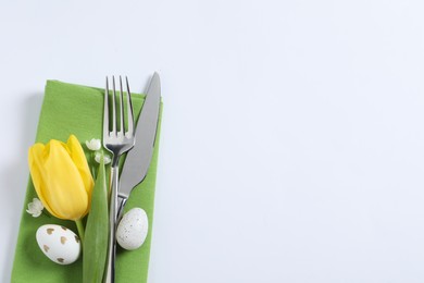 Photo of Cutlery set, Easter eggs and tulip on white background, top view with space for text. Festive table setting