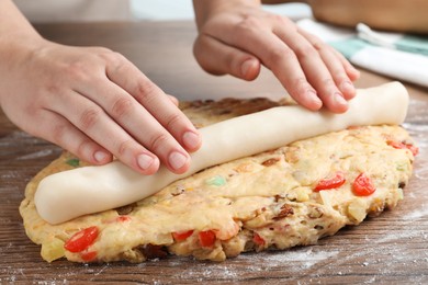 Woman putting marzipan into raw dough for Stollen at wooden table, closeup. Baking traditional German Christmas bread