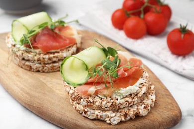 Crunchy buckwheat cakes with cream cheese, prosciutto and cucumber slices on wooden board, closeup