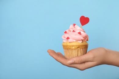 Closeup view of woman holding tasty cupcake on light blue background, space for text. Valentine's Day celebration