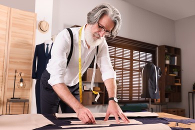 Professional tailor marking sewing pattern on fabric with chalk at table in workshop