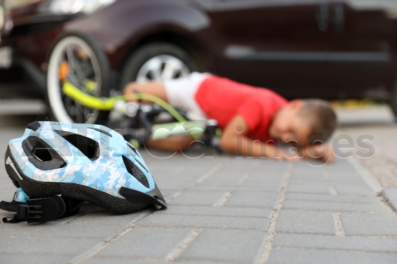 Little boy fallen from bicycle after car accident outdoors, focus on helmet