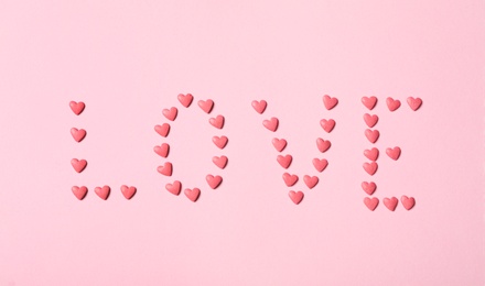 Word Love made with heart shaped sprinkles on pink background, flat lay