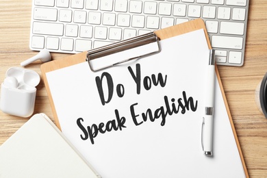 Clipboard with question Do You Speak English and stationery on wooden table, flat lay