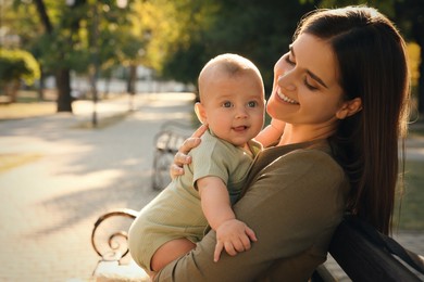 Young mother with her cute baby on bench in park
