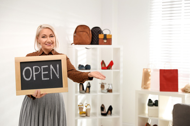 Female business owner holding OPEN sign in boutique. Space for text