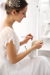 Young bride writing on her shoe indoors. Wedding superstition