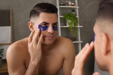 Man applying blue under eye patches near mirror at home