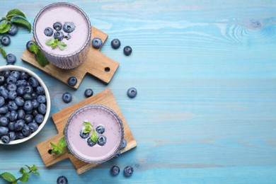 Glasses of blueberry smoothie with mint and fresh berries on light blue wooden table, flat lay. Space for text