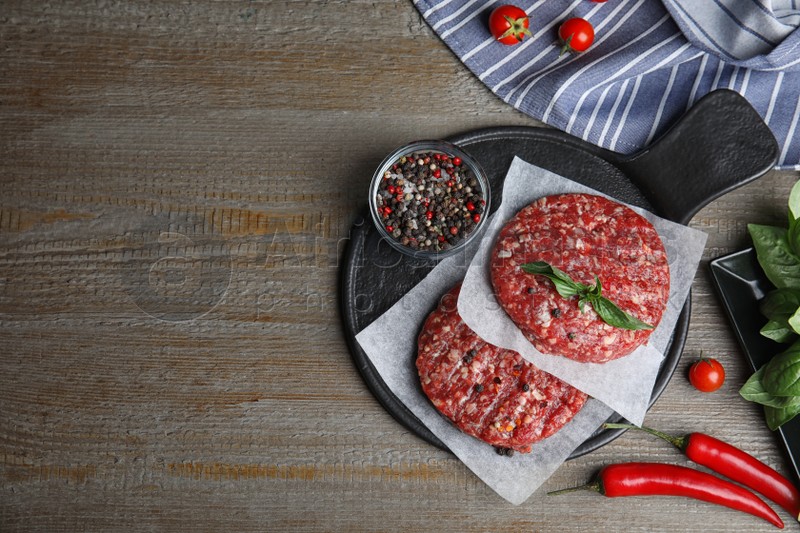 Flat lay composition with raw meat cutlets for burger on wooden table. Space for text