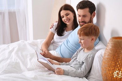 Photo of Happy parents with their child reading book on bed at home