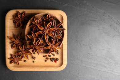 Photo of Wooden board with aromatic anise stars and spices on black table, top view. Space for text