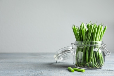 Fresh green beans in glass jar on grey wooden table, space for text