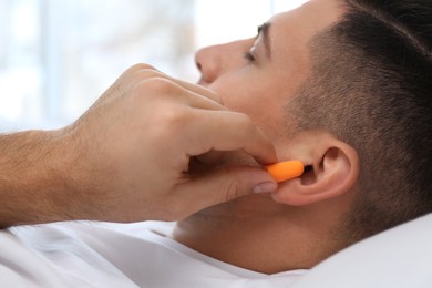Man inserting foam ear plugs in bed, closeup