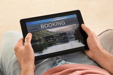 Man booking tickets online on sofa indoors, closeup. Travel agency concept